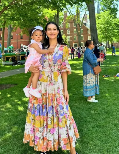Morgan Radford in a colorful spring dress holding her baby daughter on the lawn at Harvard University