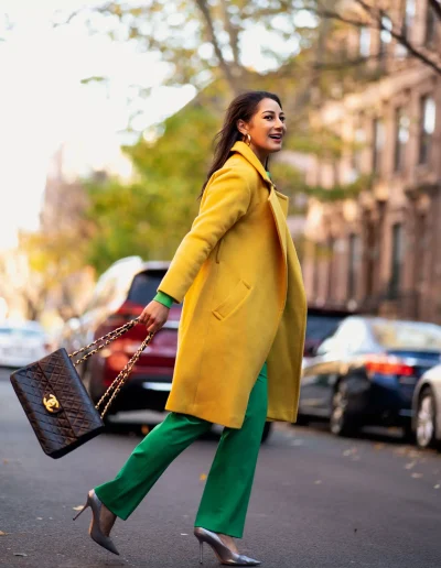 Morgan Radford crossing the street in Manhattan wearing a gold coat and green slacks